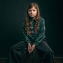 A contemplative portrait of a young girl with long hair in a dark studio setting.