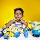 Young boy visibly excited with Minion toys in front against a vibrant yellow background.